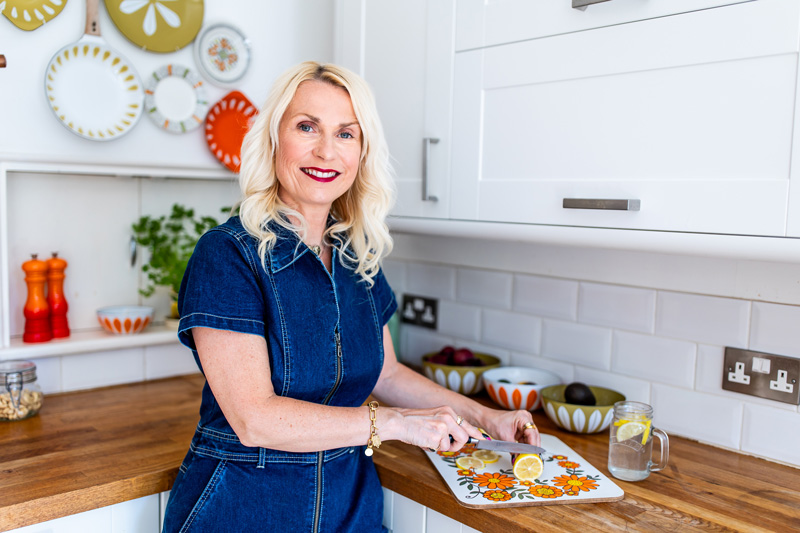 Coach posing in a kitchen with a healthy drink in hand.